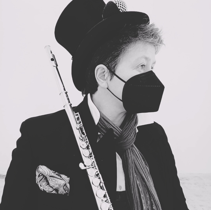 A black and white image of a person wearing a top hat and face mask holding a flute.